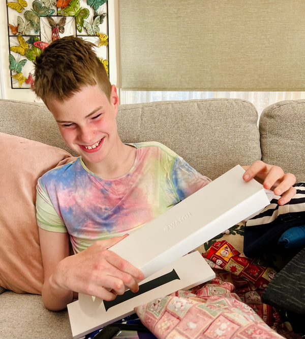 Photo of Max (13 yes old) wearing tie dye Pyjamas opening a brand new Apple Watch. He has a huge Smile on his face 