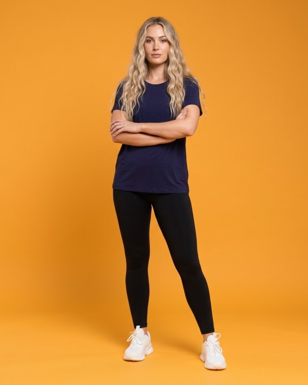 Woman wearing a navy t-shirt and black leggings on an orange background