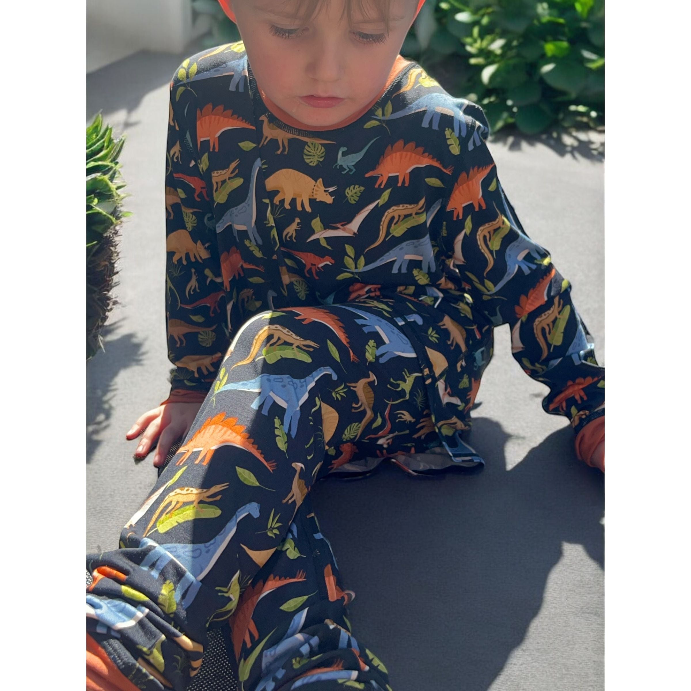 A sitting boy wearing the jurassic dreams long set - pajamas for teens from Comfort on the Spectrum.