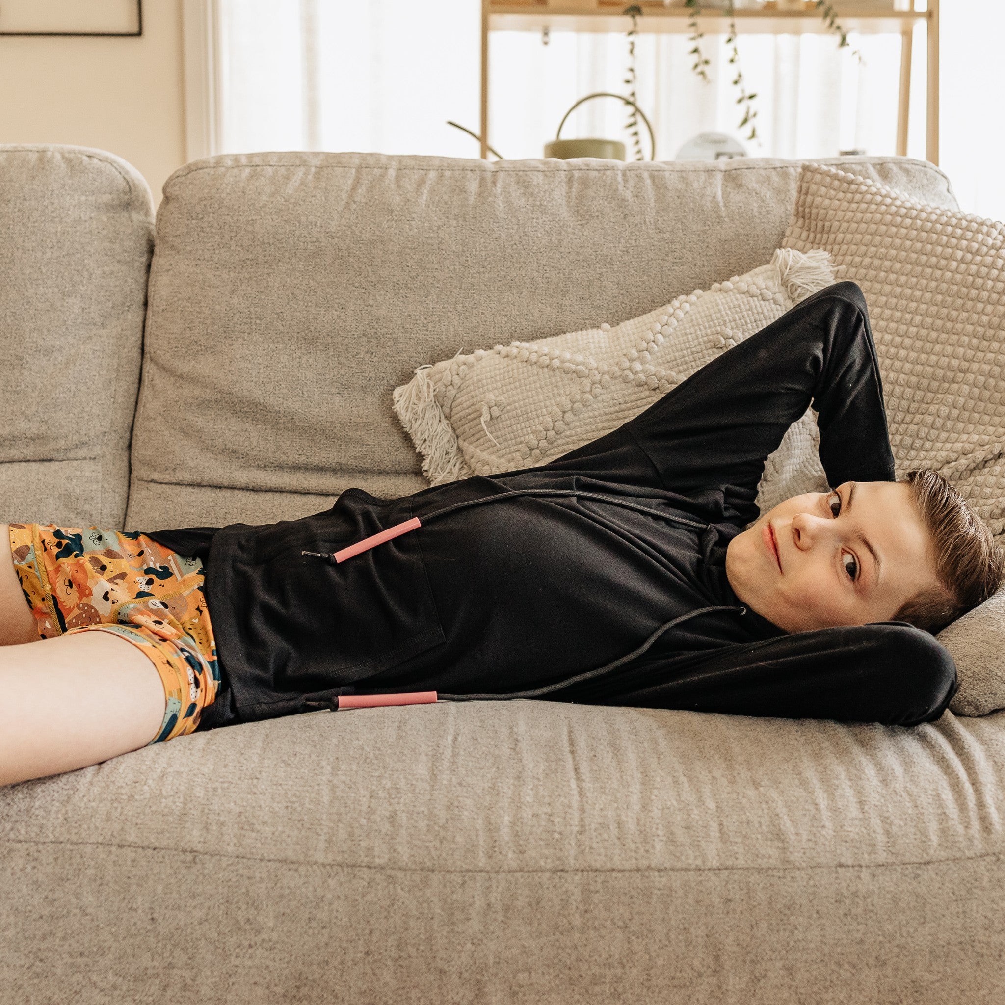Comfort on the Spectrum black bamboo-cotton blend sensory-friendly hoodie with drawstring and pouch pocket on a child lying on a couch.