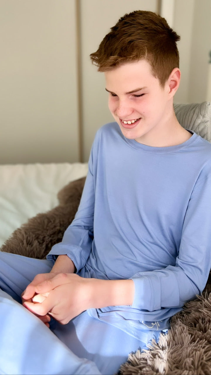 Max is sitting with his hands in his lap & a smile on his face. He is wearing our Long Set in Periwinkle 