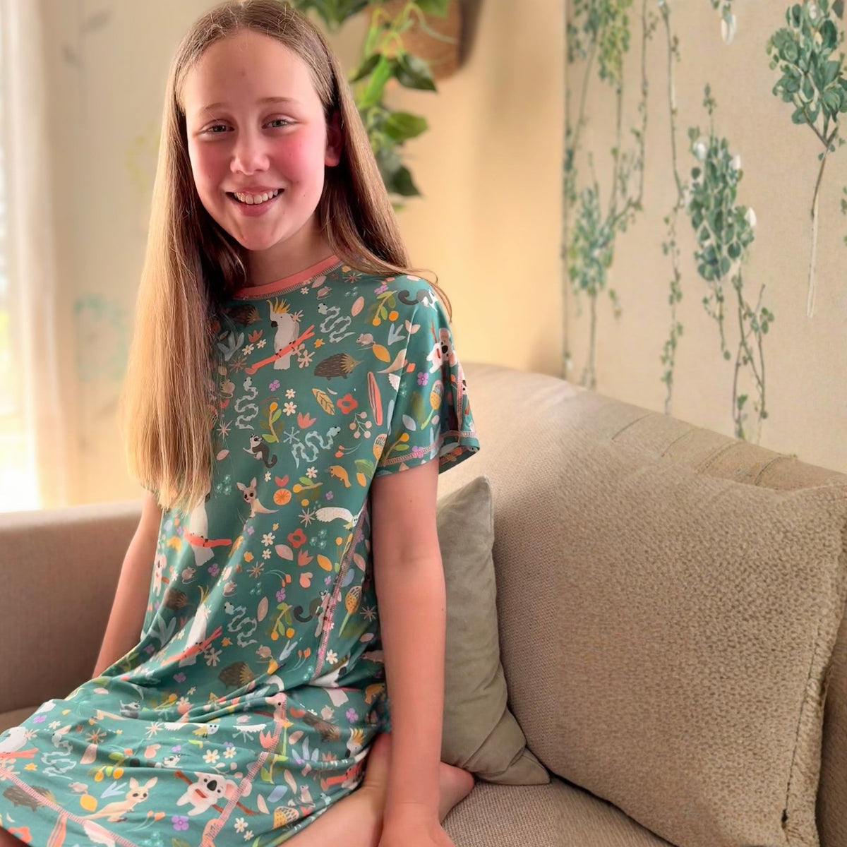 Comfort on the Spectrum green bamboo nightdress with Australian wildlife print, short sleeves, relaxed fit, worn by a smiling girl.