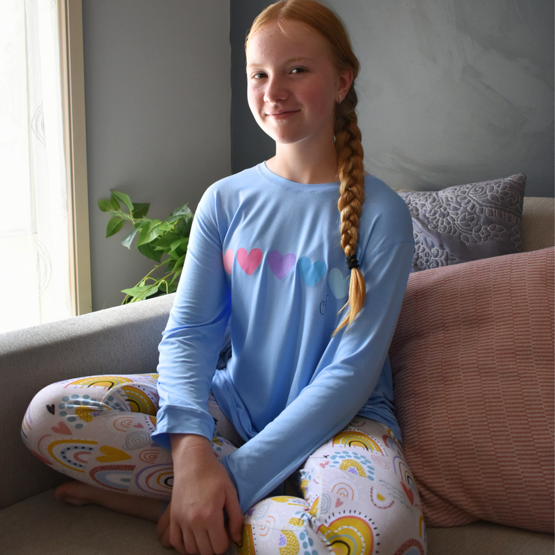 A smiling girl wearing rainbow sweatheart long set - pajama set for teens- from Comfort on the Spectrum.