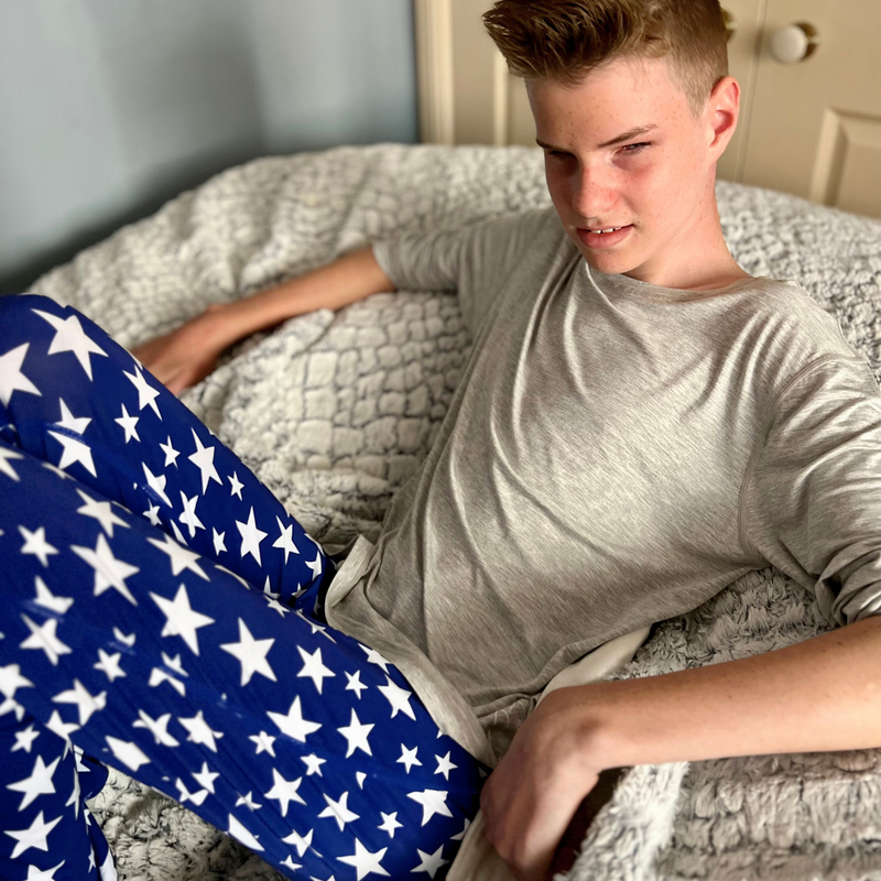 A sitting boy wearing stars  Long Set Pajamas for Teens & Kids from Comfort on the Spectrum.