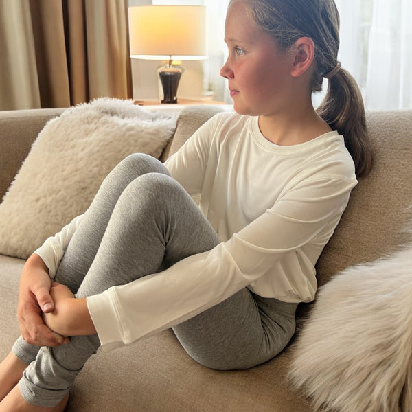 A girl sitting on the sofa wearing the grey marle sensory leggings from Comfort on the Spectrum.