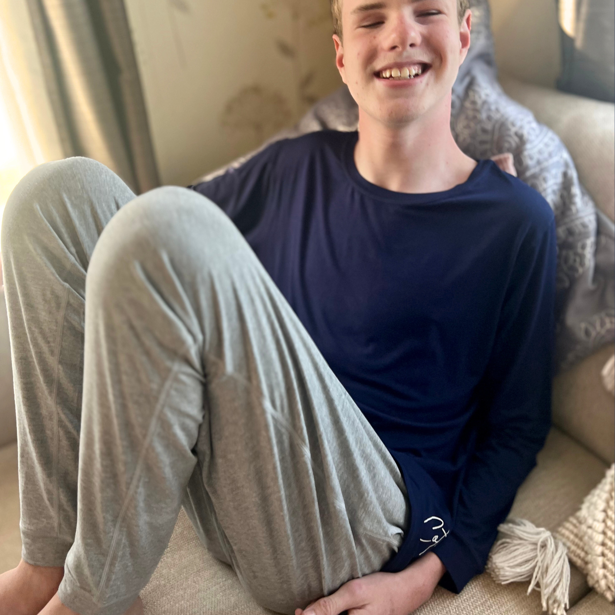 A guy sitting on the sofa while wearing the grey marle lounge pants women and men from Comfort on the Spectrum. 