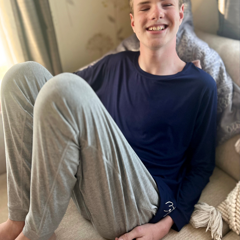 A guy sitting on the sofa while wearing the grey marle lounge pants in Australia from Comfort on the Spectrum. 