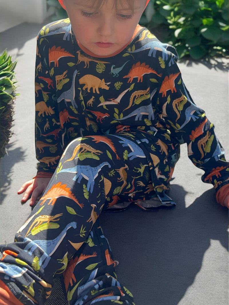 A sitting boy wearing the jurassic dreams long set - pajamas for teens from Comfort on the Spectrum.