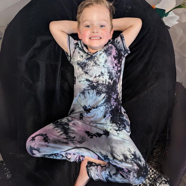 A boy wearing a cosmic splash jumpsuit pajamas for teens and kids from Comfort on the Spectrum.