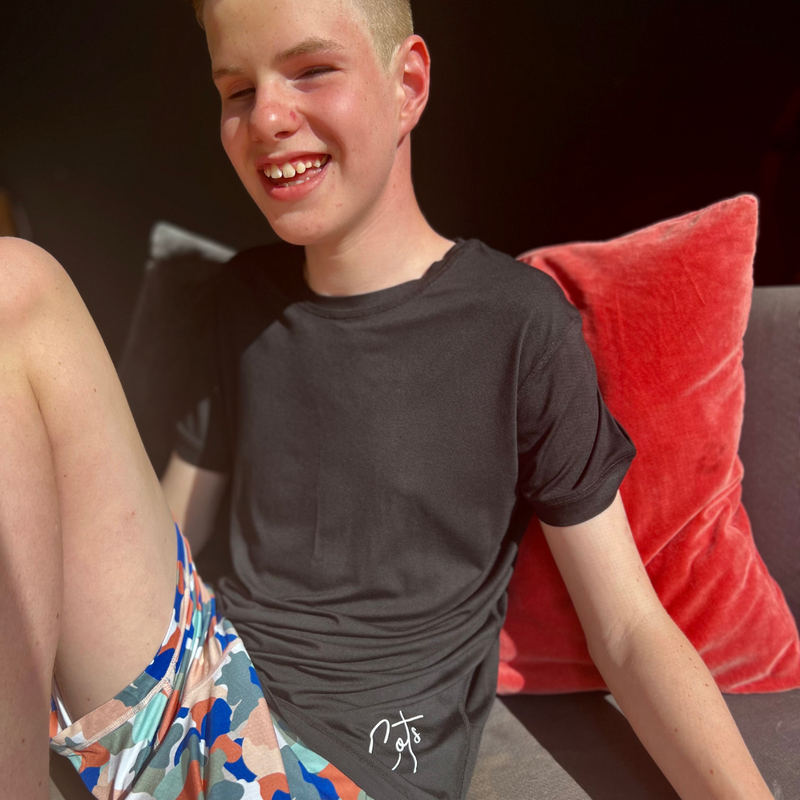 A smiling boy wearing the camo pajama short set from Comfort on the Spectrum.
